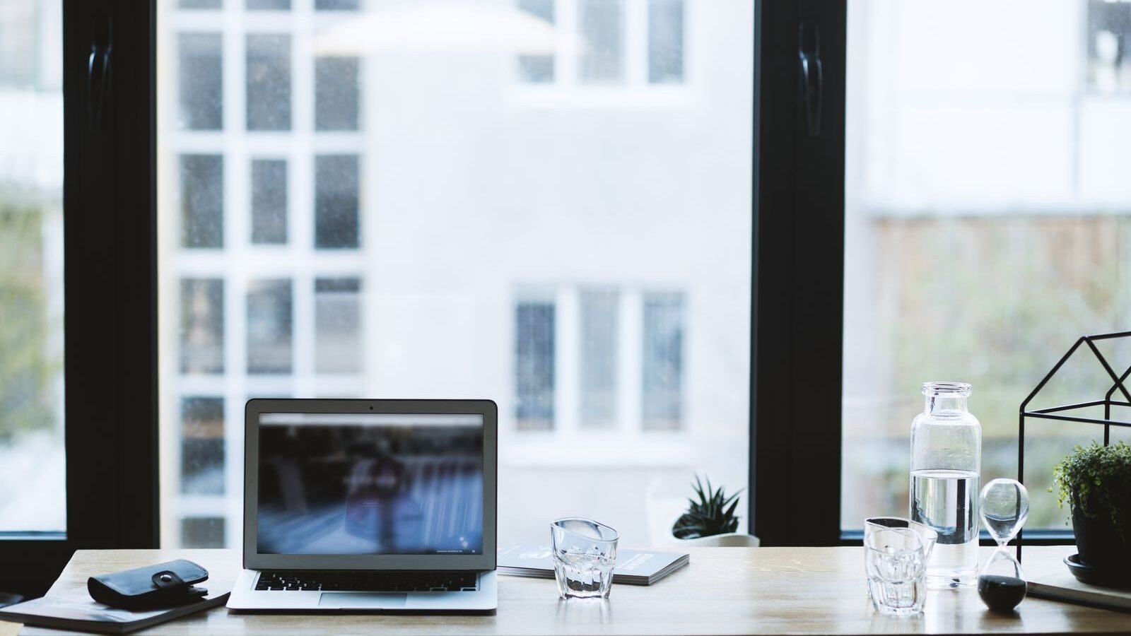 Sleek office desk setup featuring a laptop, glass of water, and open window view.